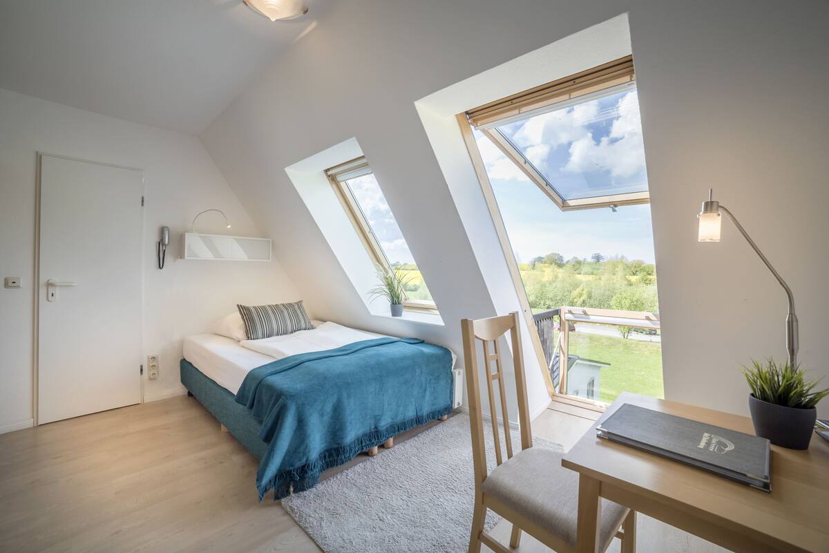A bedroom with a bed, a desk, a chair, a lamp, and a window.
