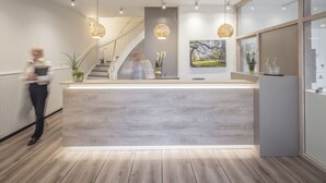 Un área de recepción moderna con un mostrador de madera, iluminación colgante, una escalera y un ventanal grande.