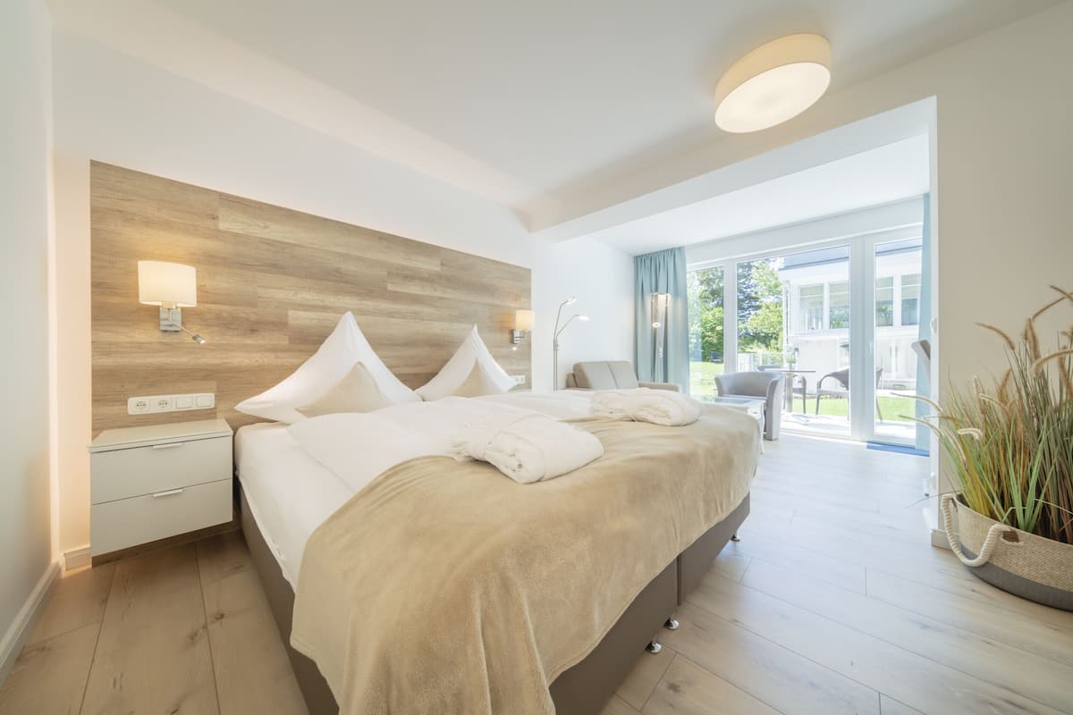 A modern bedroom with a large bed, bedside tables, a nightstand, a window with curtains, and a view of the outdoors.