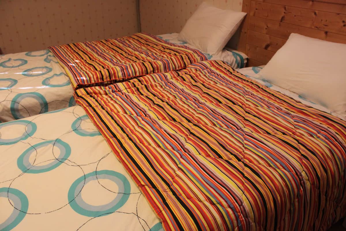 A room with two beds, each with a striped bedspread and circular patterns on the pillows.