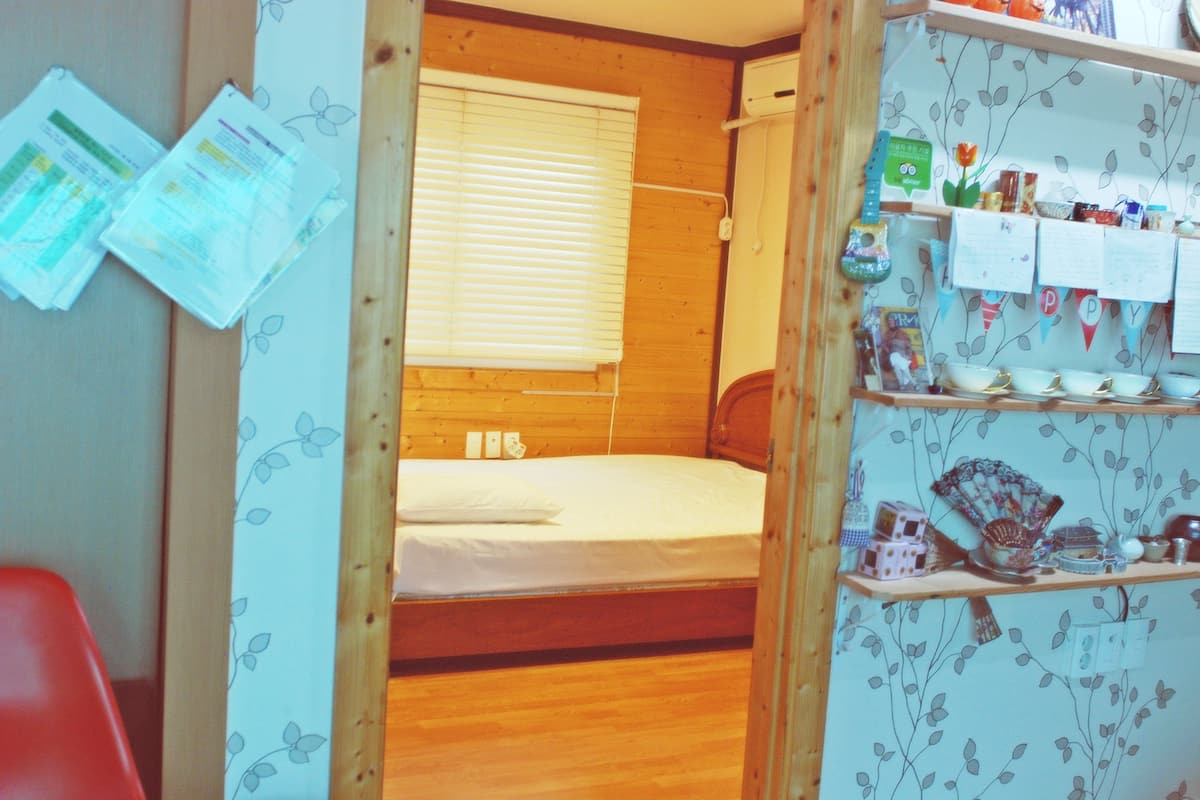 A small, cozy room with a wooden bunk bed, a shelf with various items, and a wall with papers and notes.