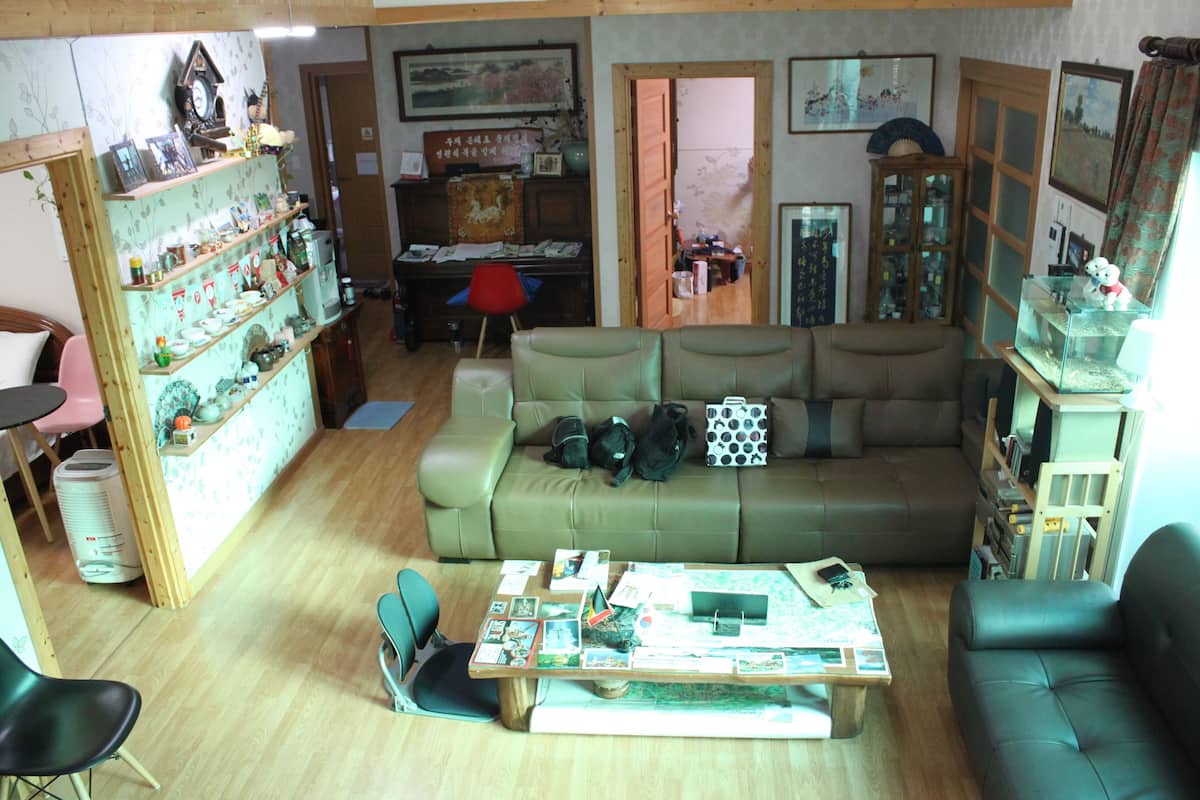 A cozy living room with a sofa, a coffee table with various items, a bookshelf, and a door leading to another room.