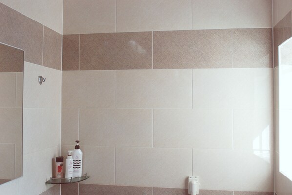Un baño con baldosas color beige, un estante de vidrio con artículos de aseo y un secador de manos.