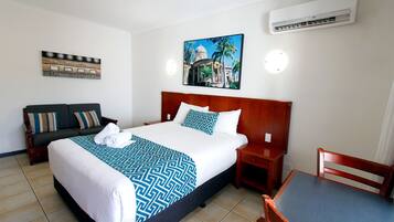 Une chambre d’hôtel avec un grand lit, une table de chevet en bois, une chaise en bois, une petite table, un canapé et un climatiseur fixé au mur.