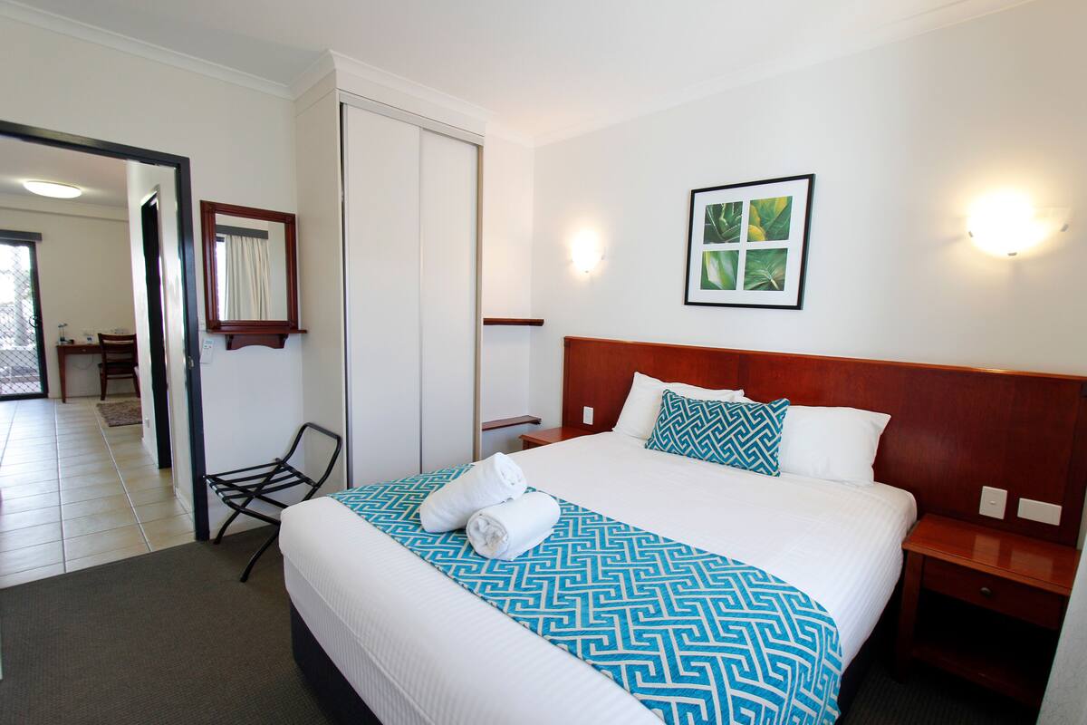 A hotel room with a large bed, a wooden headboard, a nightstand, a chair, and a wall-mounted picture.