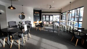 A modern dining area with black and grey furniture, large windows, and a ceiling fan. - Coffee House Apartment Motel (Rockhampton)
