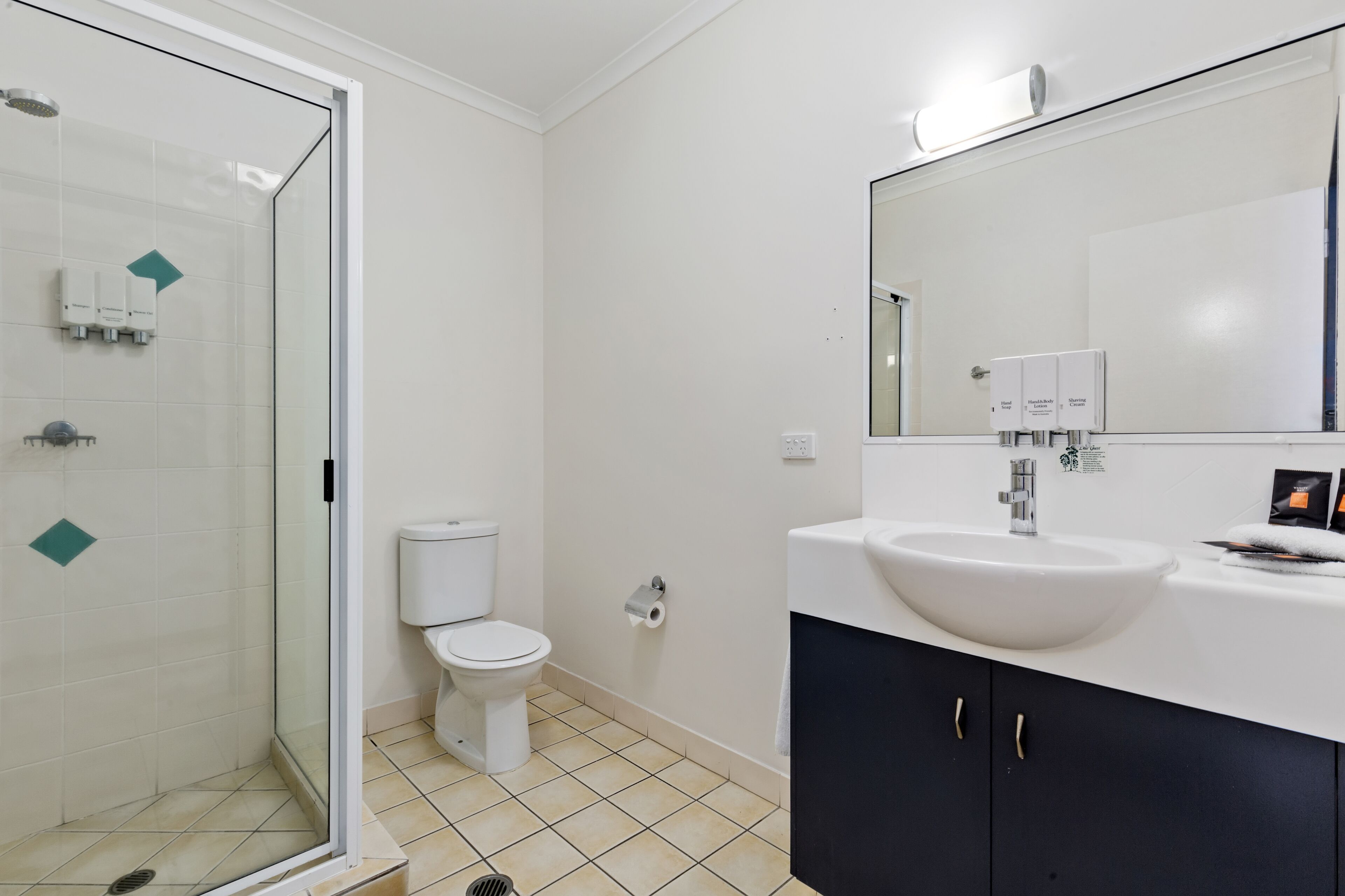 Un baño moderno con ducha de vidrio, inodoro blanco, lavamanos blanco y un espejo grande.