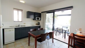 A compact kitchen with a dishwasher, a microwave, and a sink. There is a dining area with a table and chairs. - Coffee House Apartment Motel (Rockhampton)