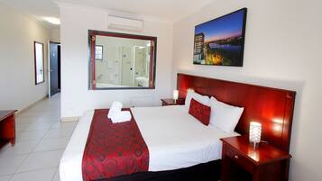 Habitación de hotel con una cama grande, una mesita de noche con lámpara, un espejo y un cuadro en la pared.