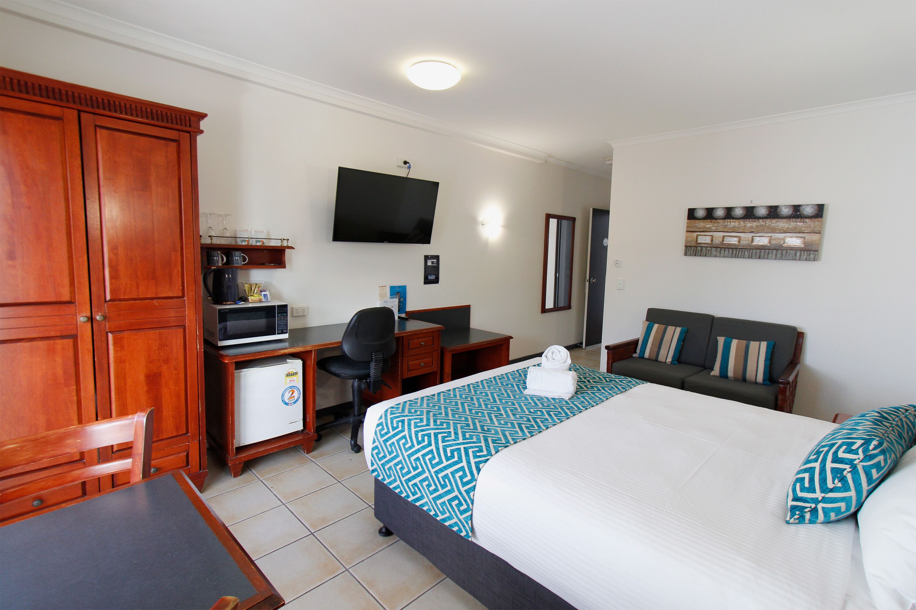 A hotel room with a bed, a desk, a chair, a television, and a wardrobe.