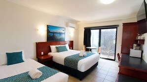 A hotel room with two beds, a TV, a desk, and a balcony with a view. - Coffee House Apartment Motel (Rockhampton)