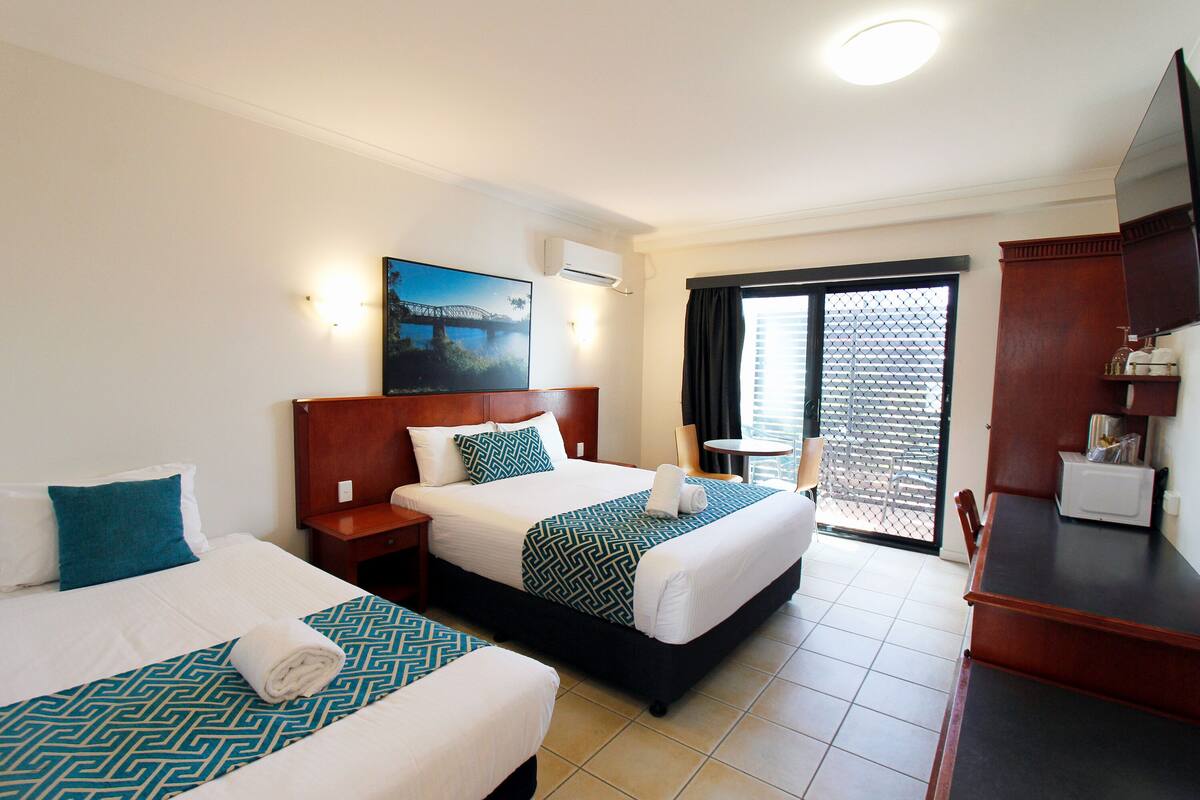 A hotel room with two beds, a TV, a desk, and a balcony with a view.