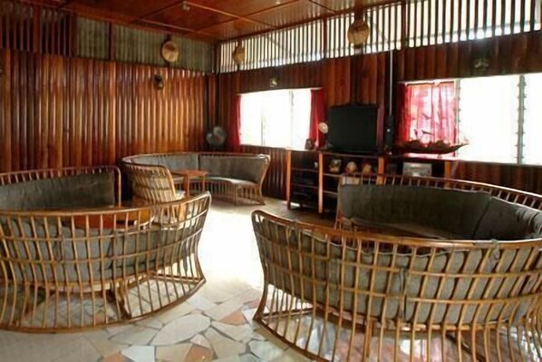 A room with wicker furniture, a television, and a window with red curtains. - Sepilok Jungle Resort (Sandakan)