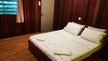 A room with a wooden floor, a bed with a white bedspread and pillows, a door, and a window with curtains.