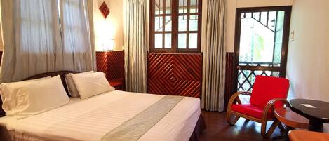 Une chambre d’hôtel avec un lit, une chaise, une table et une fenêtre avec des rideaux.
