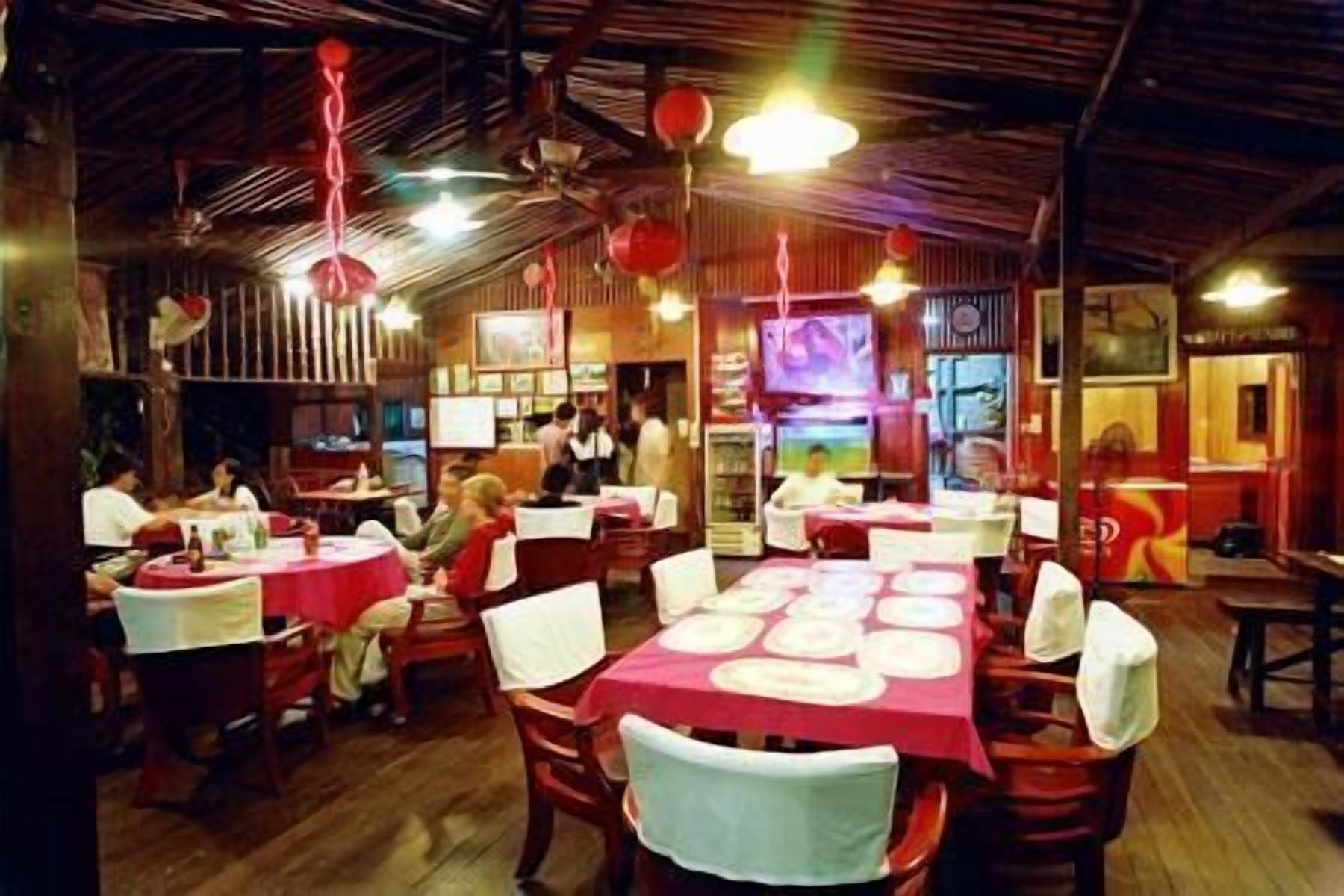 Un restaurant avec des tables et des chaises en bois, des lanternes rouges et un écran de télévision.