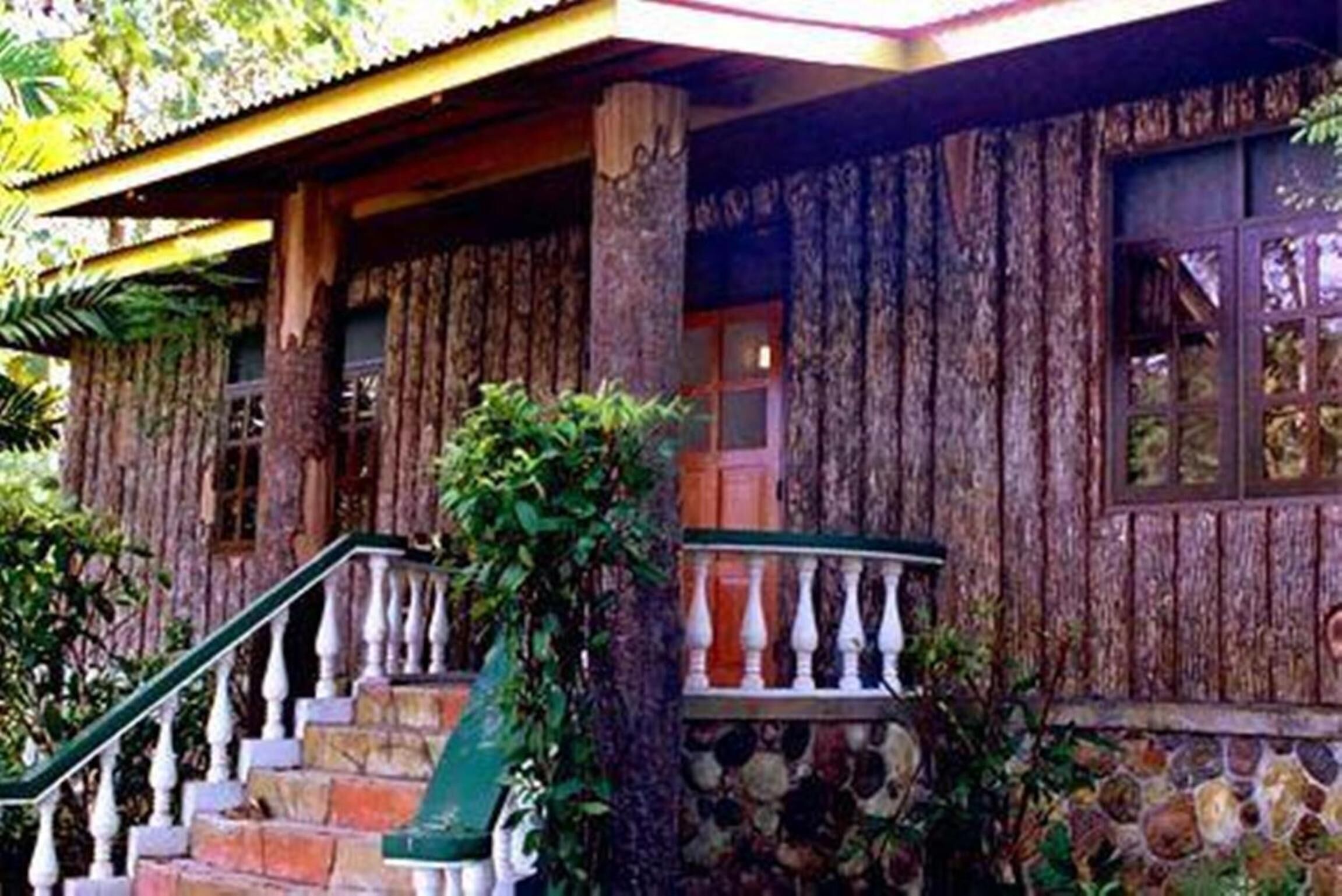 A wooden building with a stone base, a staircase with white balusters, and a window with curtains.