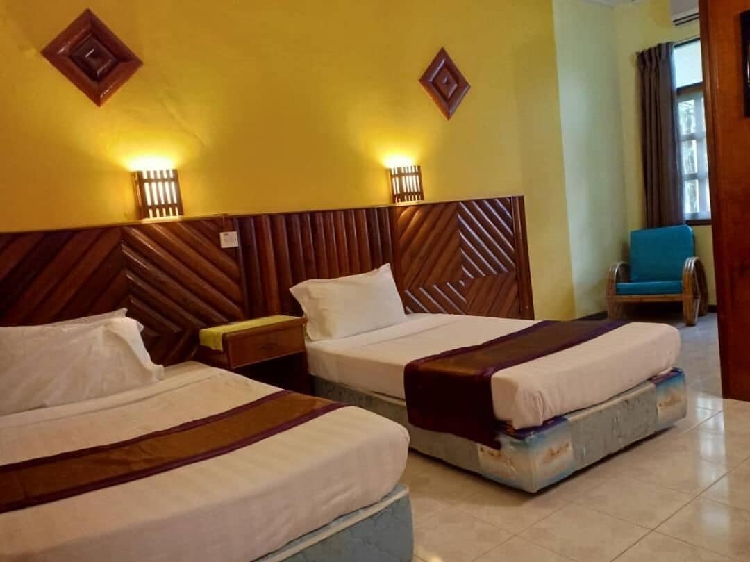 A hotel room with two beds, wooden headboards, and wall-mounted lights.