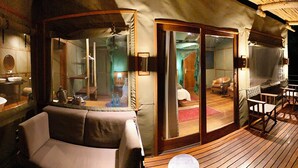 A private suite with a glass-enclosed bathroom, a seating area with a table, and a view of the deck. - Ndhovu Safari Lodge - Campground (Mahango)