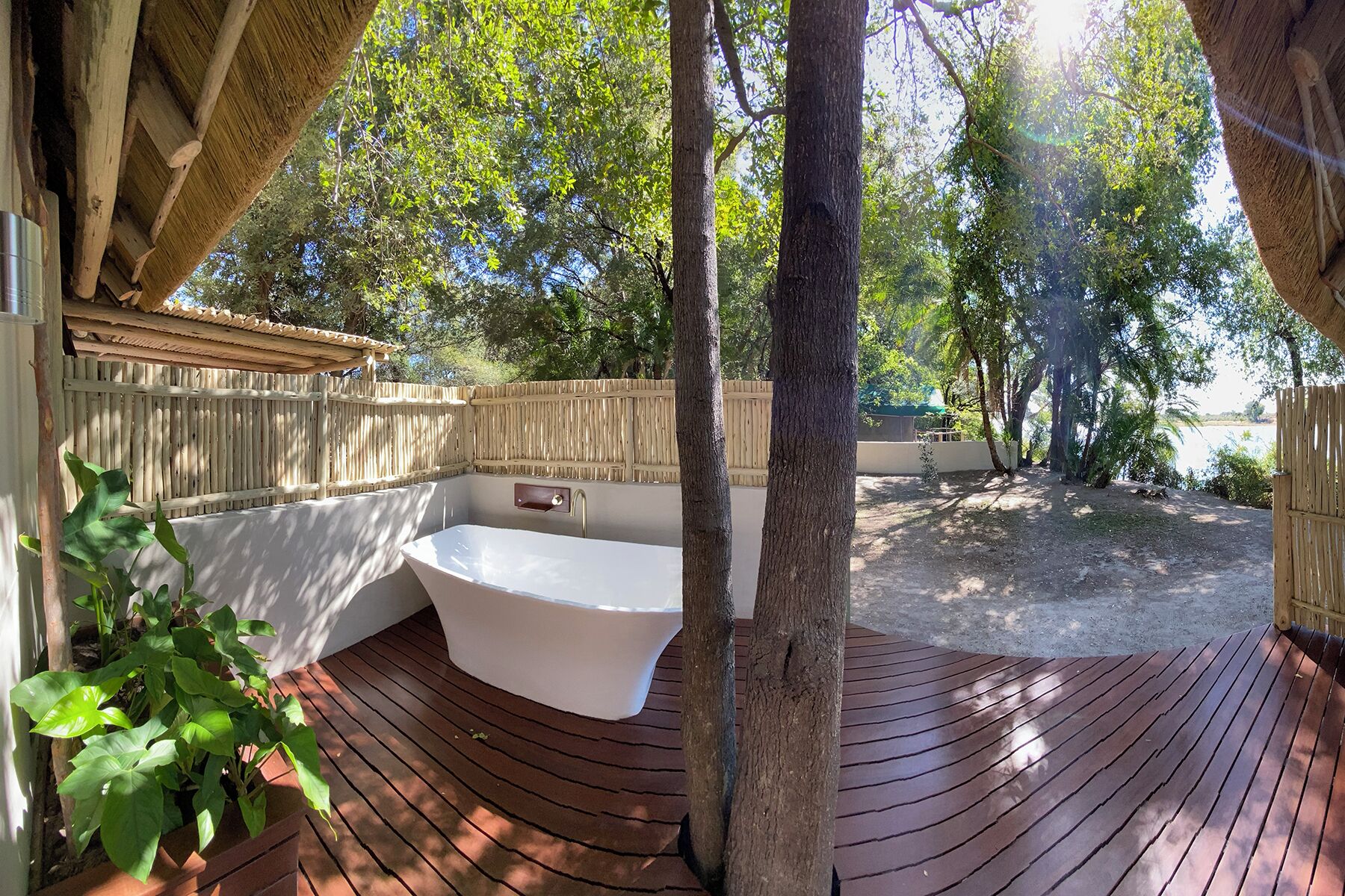 Una terraza de madera con una bañera blanca, rodeada por una valla de madera y árboles.