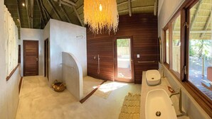 A modern bathroom with a large bathtub, a sink, and a shower. There is a hanging light fixture above the bathtub. - Ndhovu Safari Lodge - Campground (Mahango)