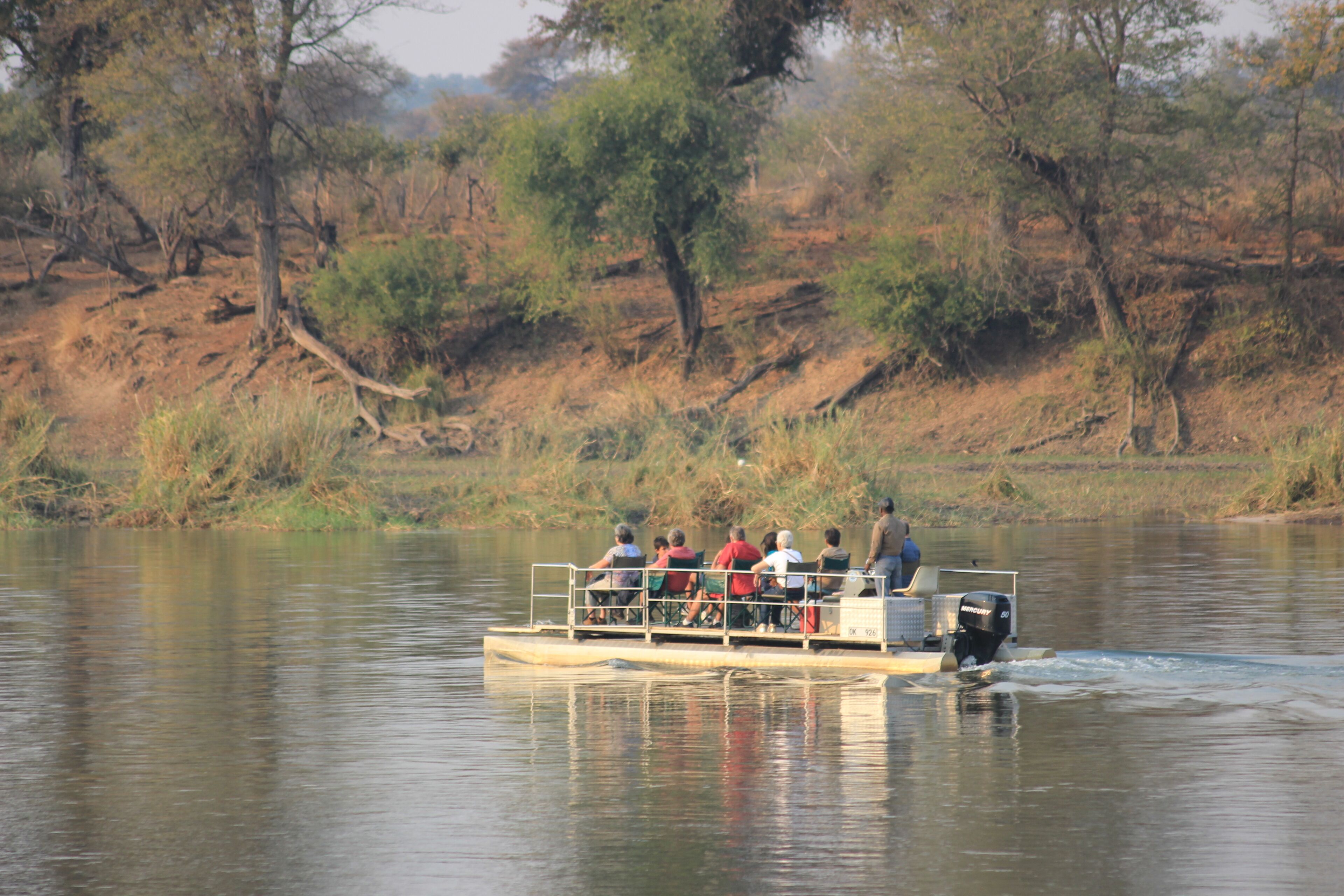 Un bote con pasajeros en un río tranquilo rodeado de árboles.