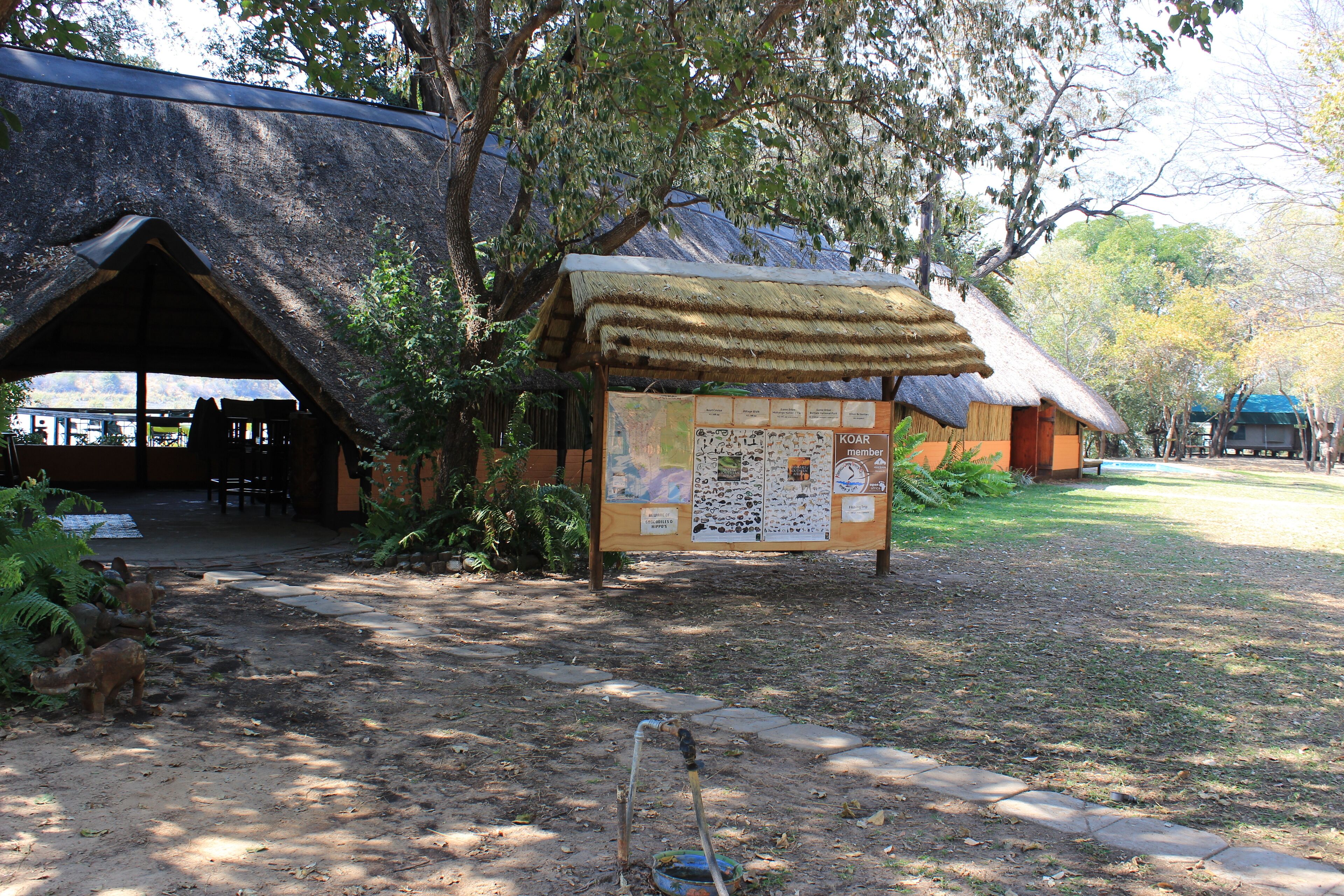 Un espacio rústico al aire libre con cabañas de techo de paja y un letrero de madera.
