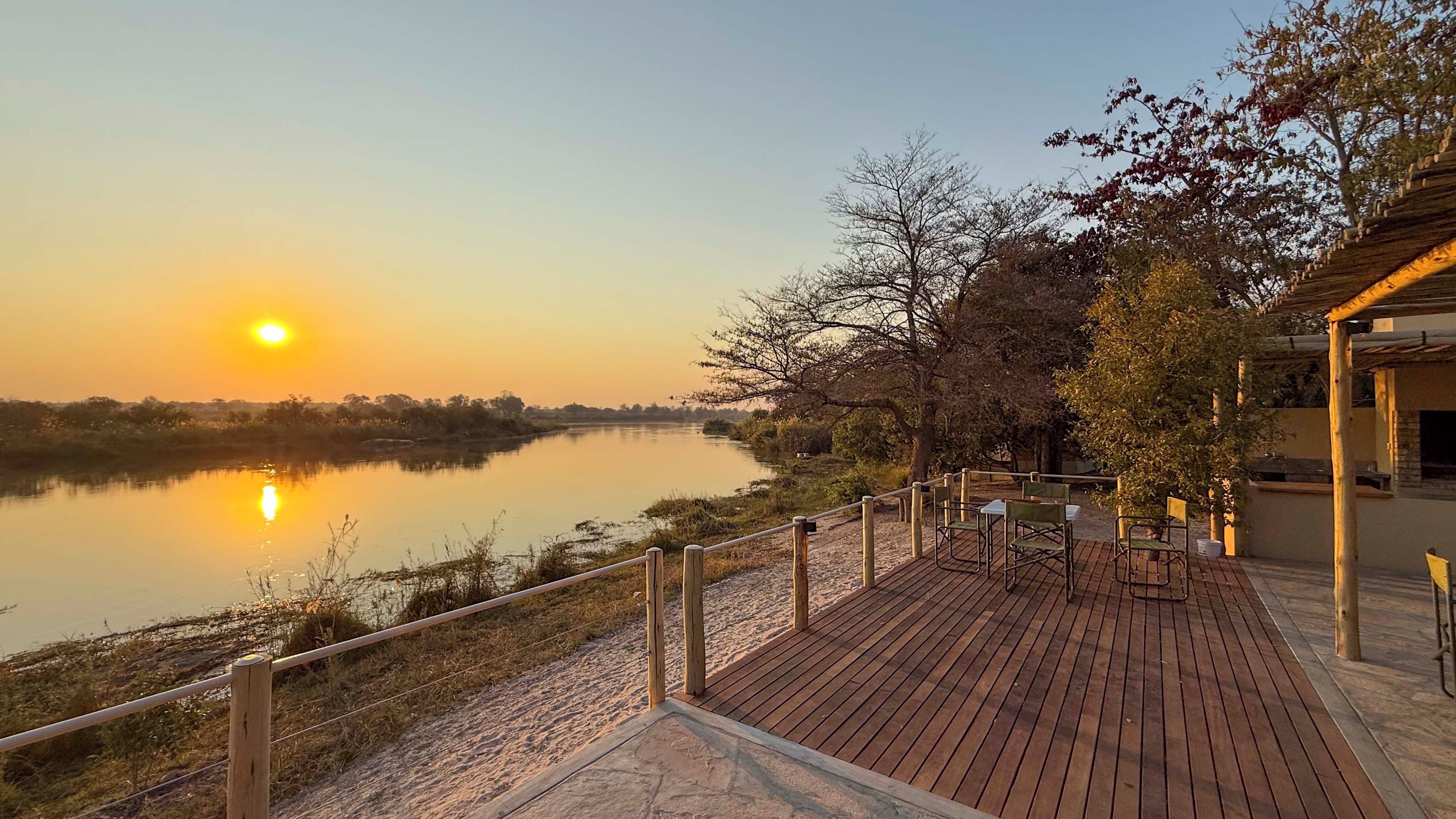 Una terraza de madera con sillas que da a un río tranquilo durante el atardecer.
