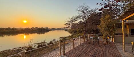 Una terraza de madera con sillas que da a un río tranquilo durante el atardecer.