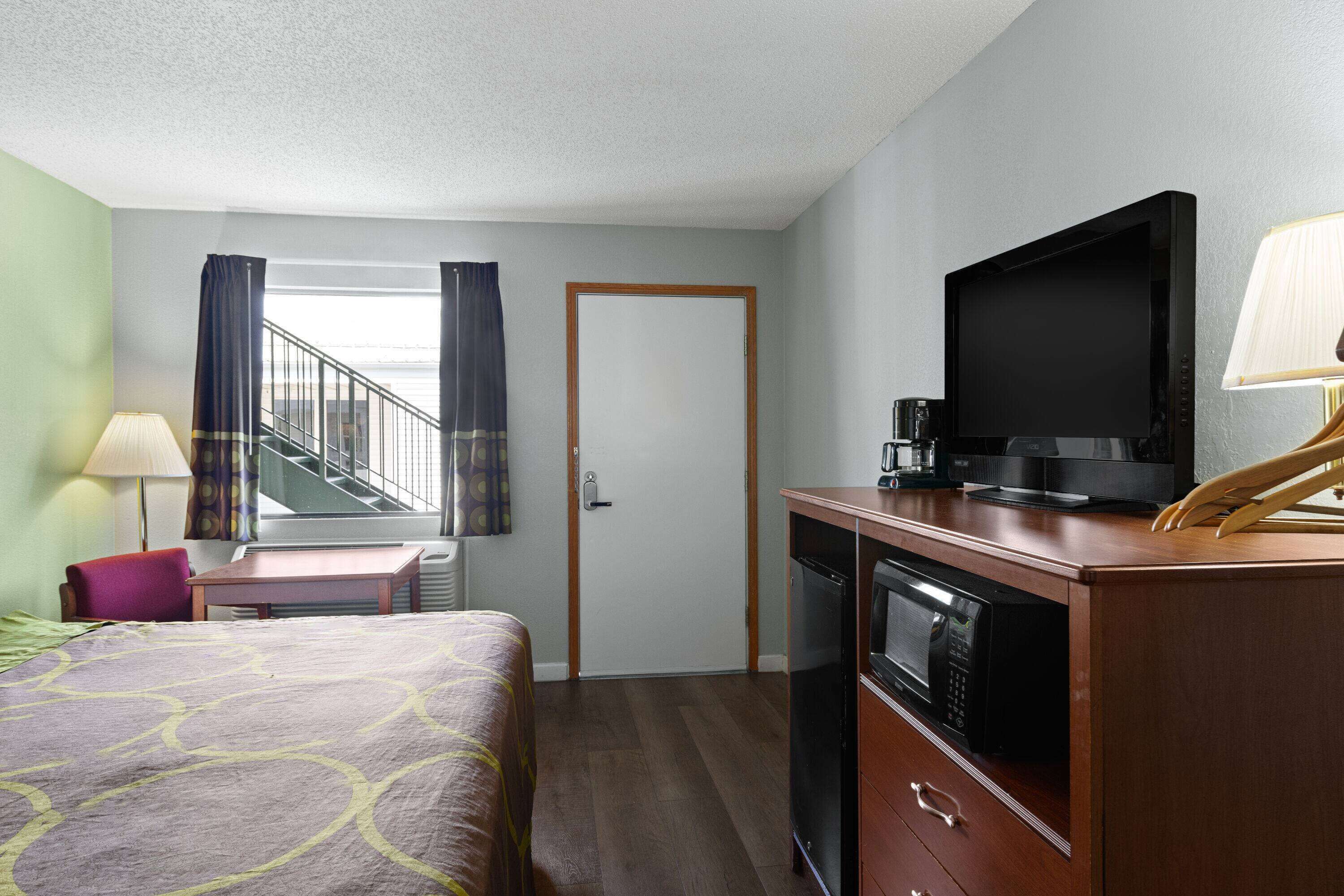 A hotel room with a bed, a desk, a television, a microwave, and a staircase visible through a door.