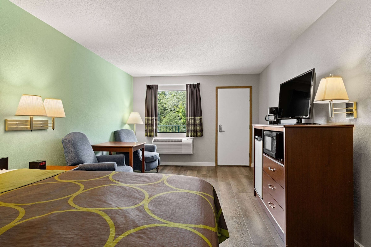 A hotel room with a bed, a desk, a chair, a television, and a dresser.