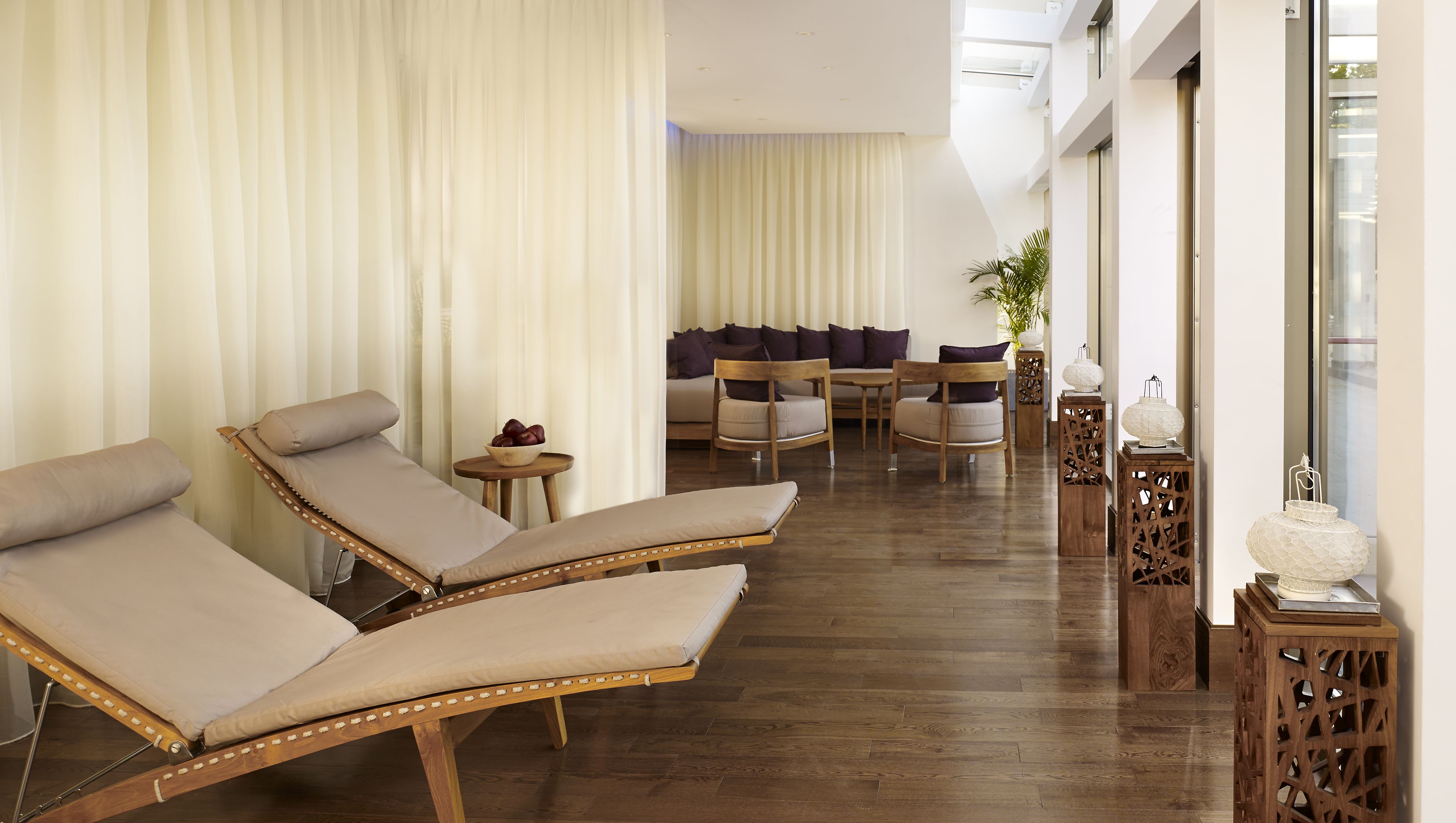 A sunlit room with two lounge chairs, a sofa, and a small table with a bowl of fruit.
