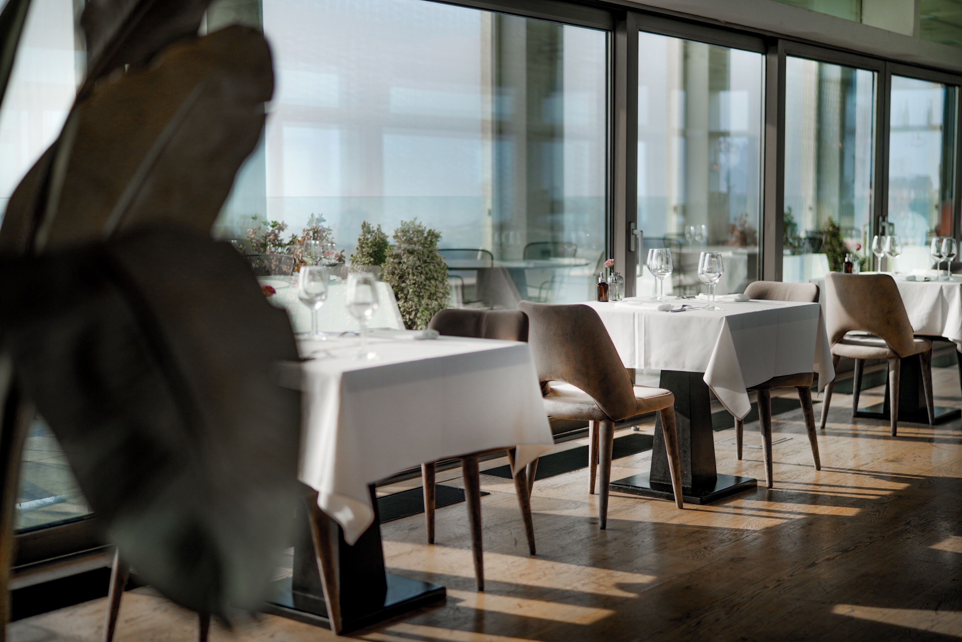 Un restaurant avec des tables dressées pour le service, de grandes fenêtres et une vue sur la ville.