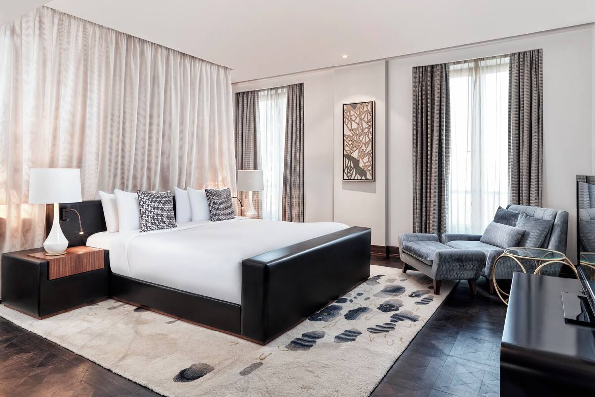 A modern hotel room with a large bed, two bedside tables, a sofa, and a TV.