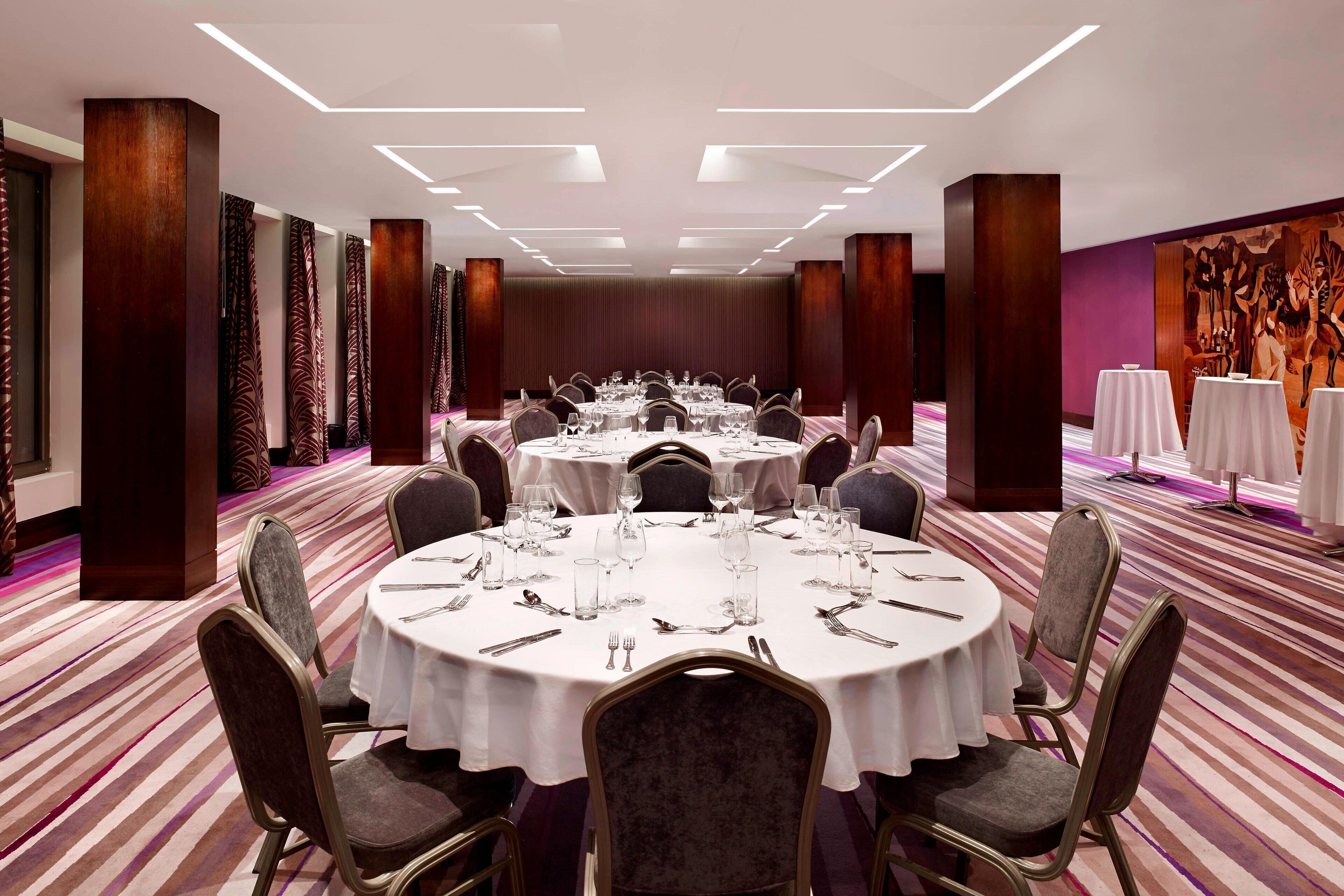 A conference room with round tables, chairs, and a carpeted floor.