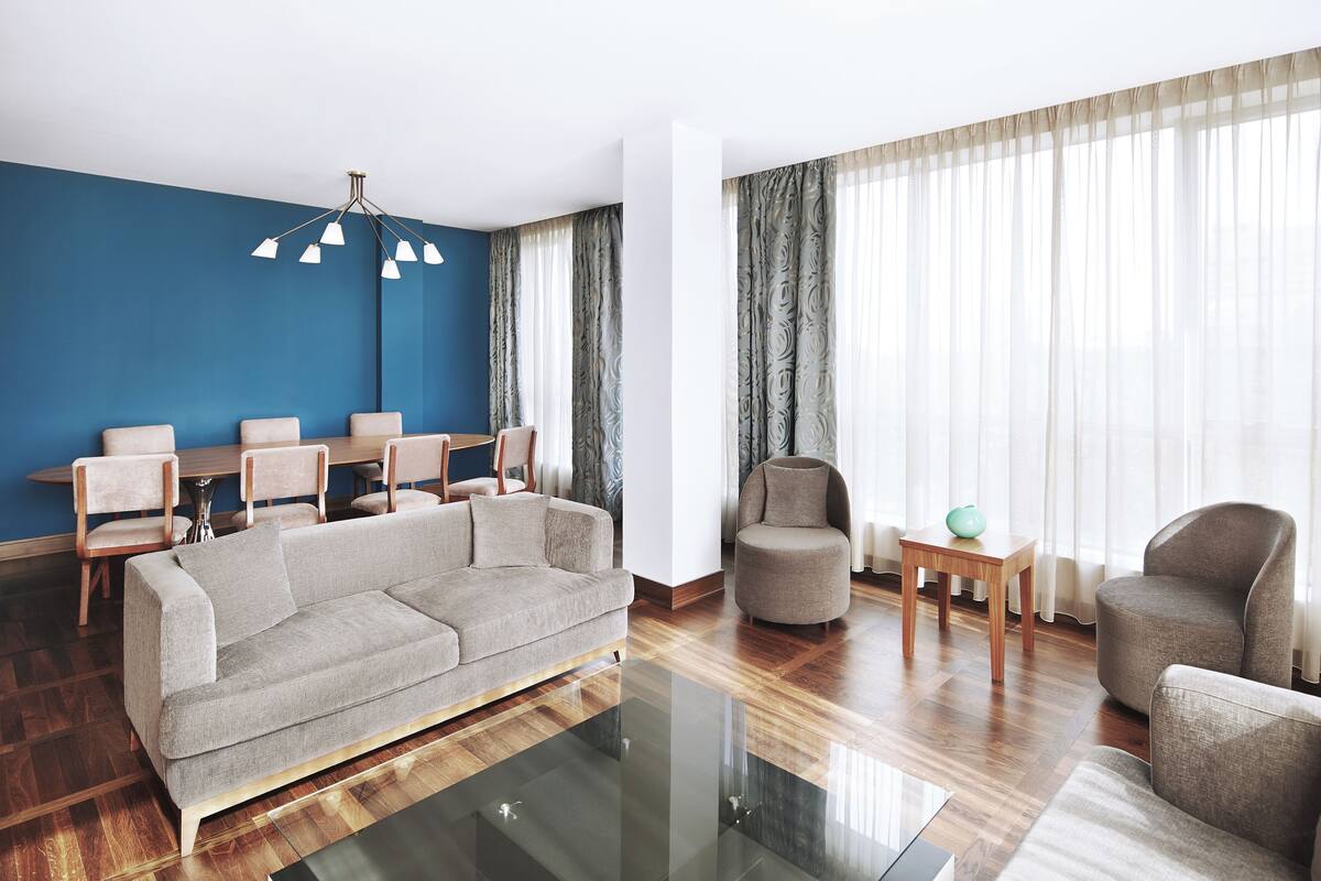 A modern living room with a grey sofa, wooden chairs, a glass coffee table, and a blue accent wall.