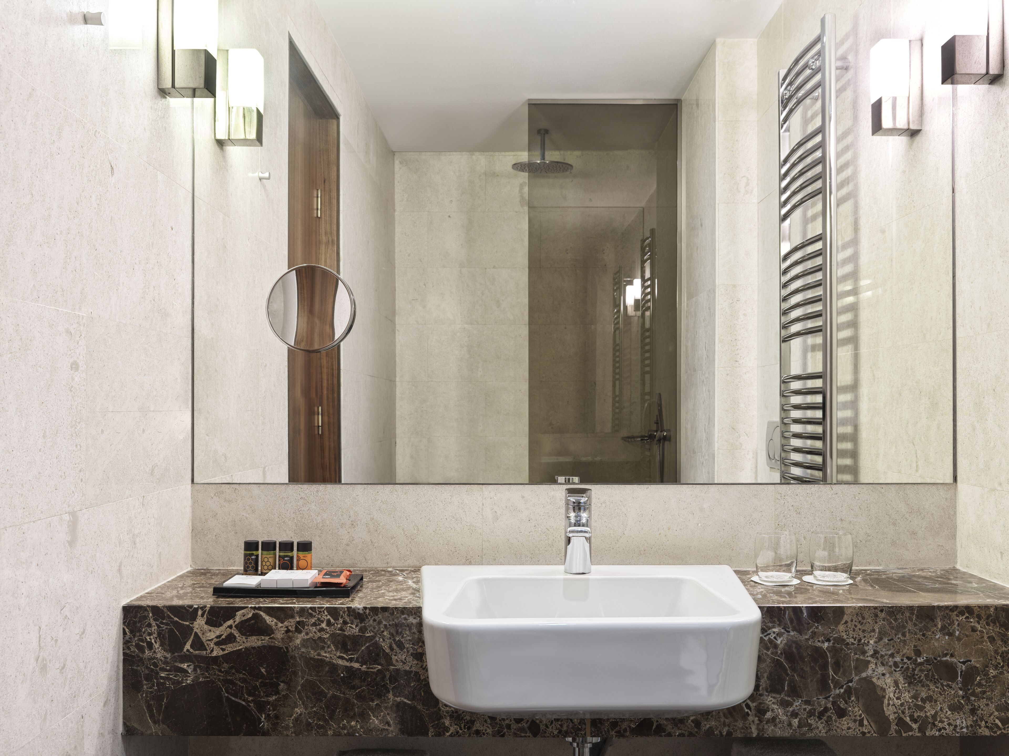 A modern bathroom with a marble sink, a large mirror, and a glass shower enclosure.