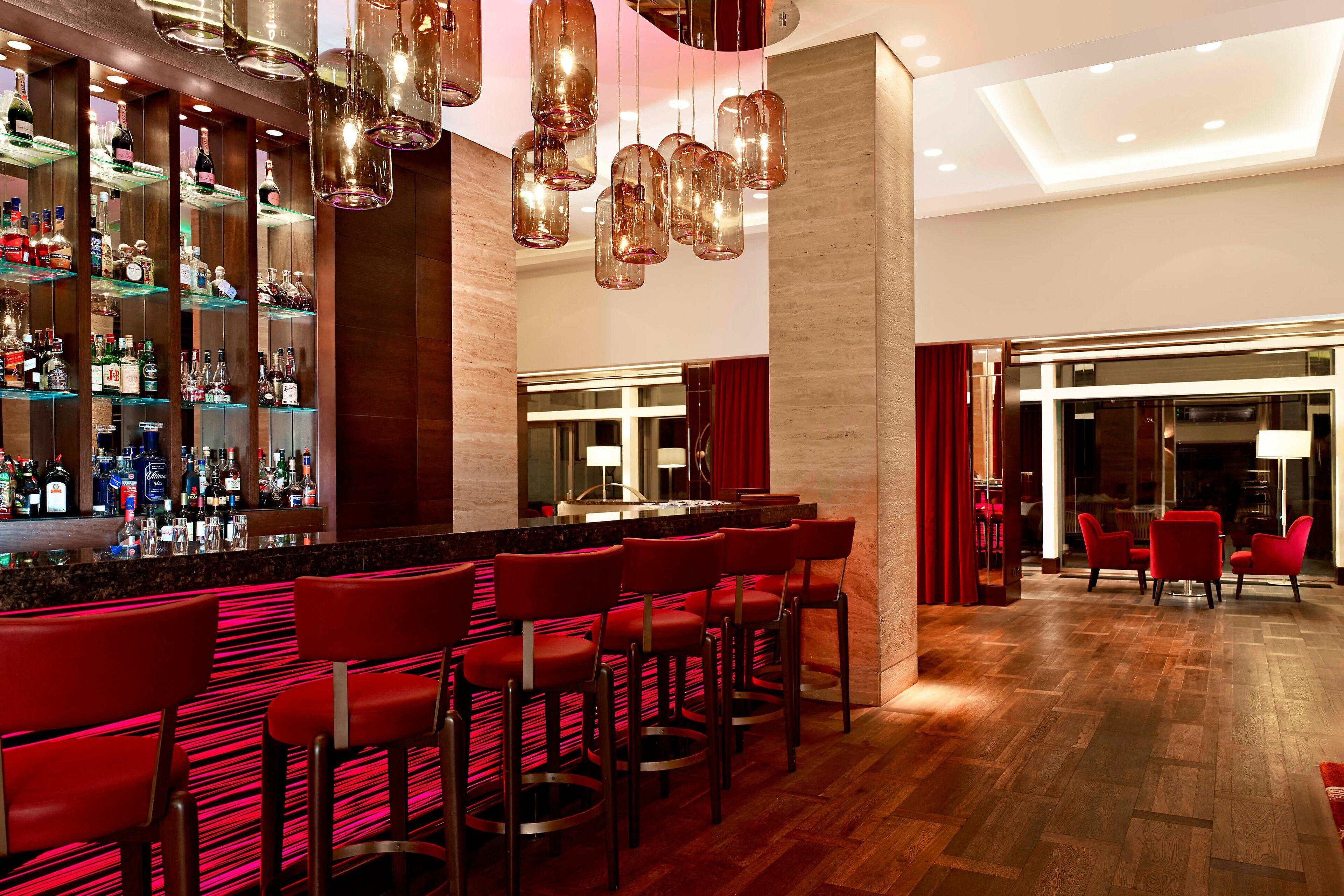 A bar area with red bar stools, a well-stocked liquor shelf, and hanging pendant lights.