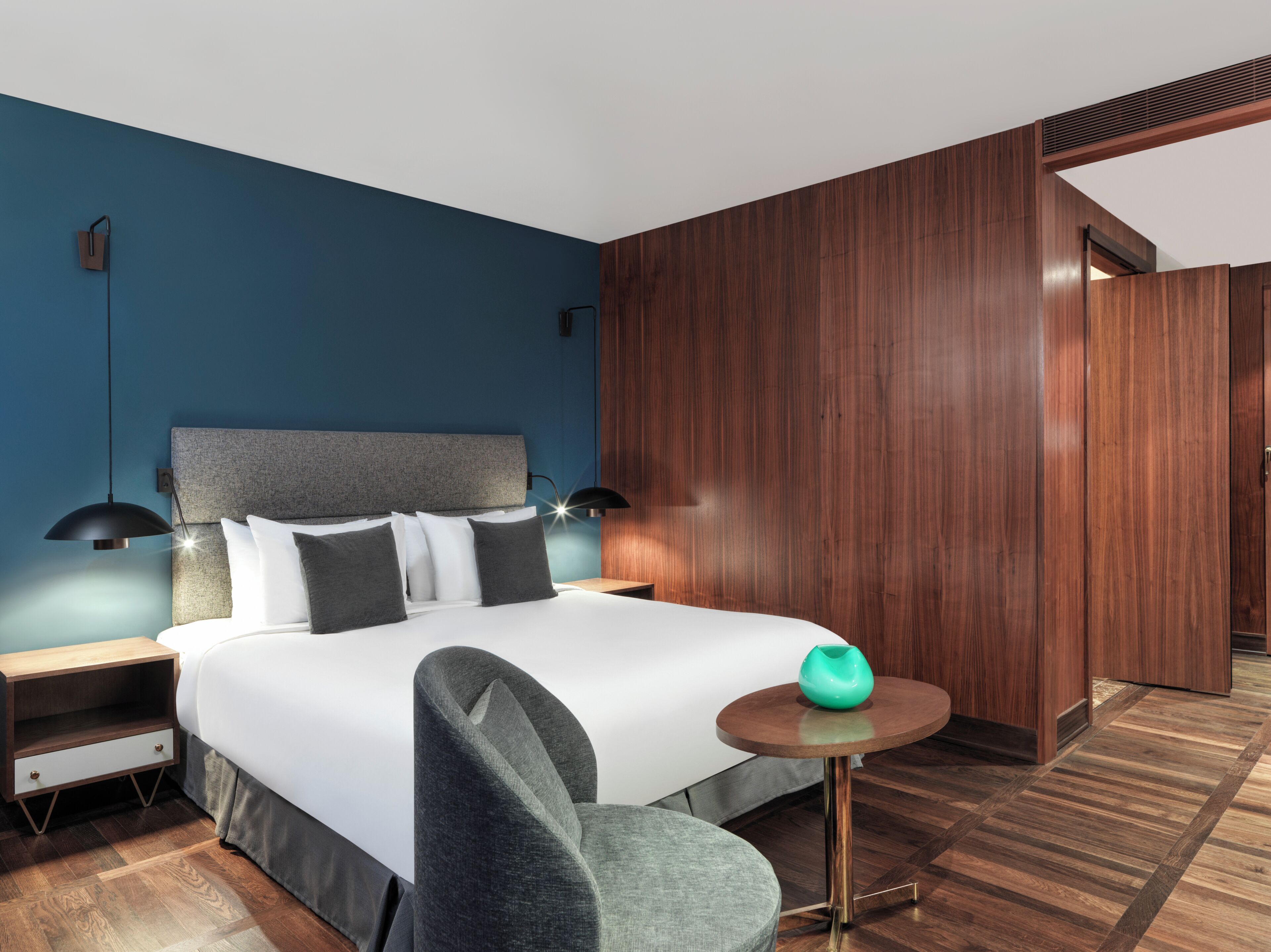 A modern hotel room with a bed, bedside tables, a round table, and a chair.