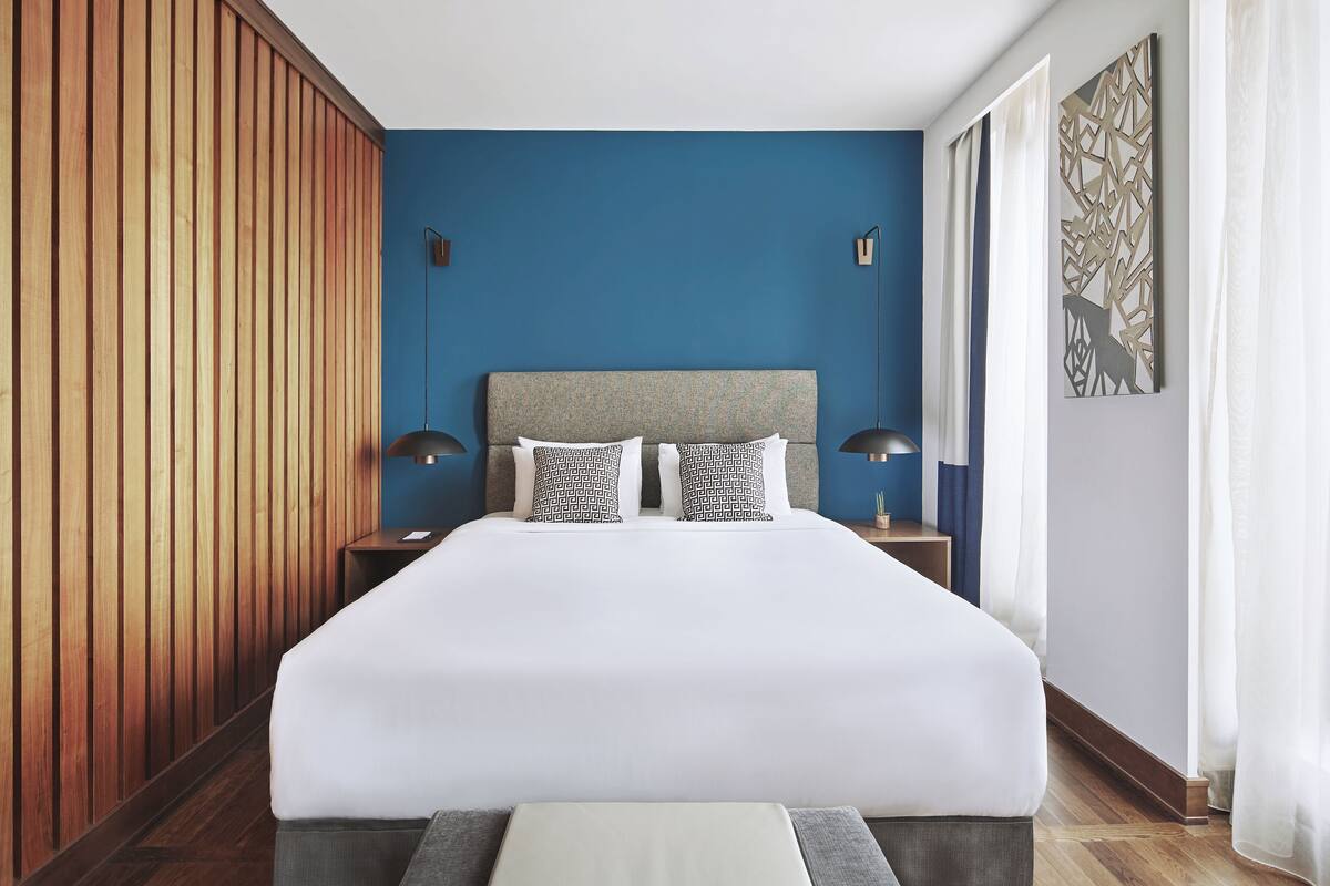 A hotel room with a large bed, wooden paneling on one wall, and a blue accent wall.