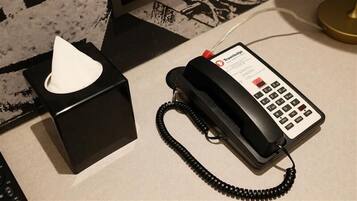 A black telephone with a cord, a tissue box, and a Travelodge logo on the phone.