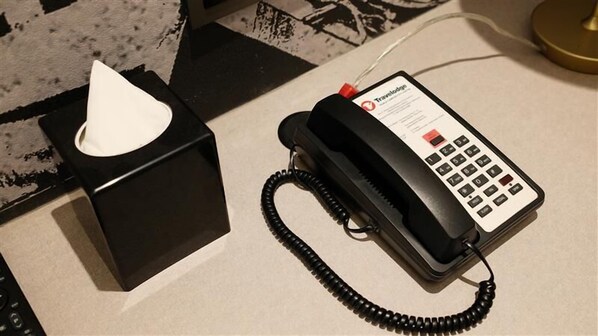 Un teléfono negro con cable, una caja de pañuelos y el logotipo de Travelodge en el teléfono.
