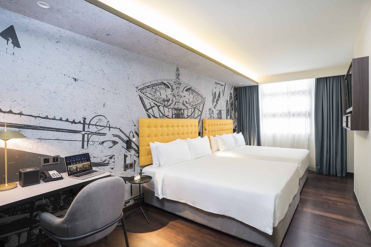 Une chambre d’hôtel avec un grand lit, un bureau avec un ordinateur portable, une chaise et un mur orné d’une fresque.