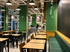 L’intérieur d’un restaurant avec des murs recouverts de carreaux verts, des tables en bois et des chaises noires.