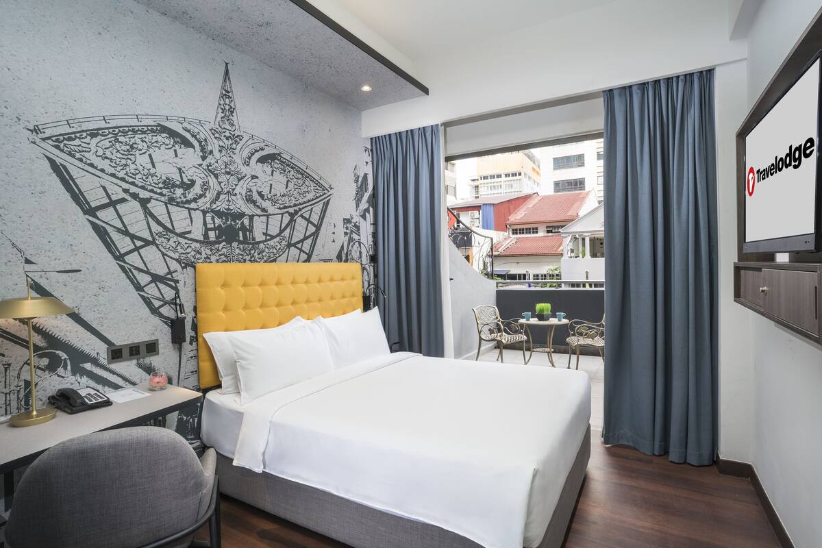 Une chambre d’hôtel avec un lit, un bureau doté d’une lampe, une chaise, un téléviseur et un balcon offrant une vue sur les bâtiments.