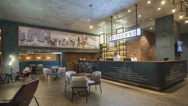 Een modern café met een receptiebalie, een zithoek en een stadsgezicht muurschildering.