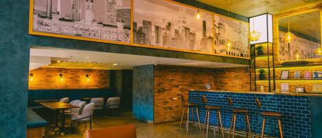 A restaurant with a high ceiling, exposed brick walls, and a cityscape mural. There are booths, a bar area with stools, and a counter with a menu.