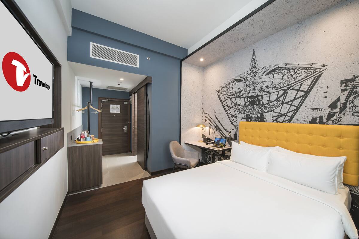 Une chambre d’hôtel équipée d’un lit, d’un bureau, d’une chaise, d’une télévision et d’un mur orné d’une fresque.