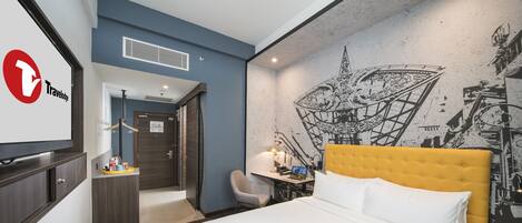 A hotel room with a bed, a desk, a chair, a TV, and a wall with a mural.