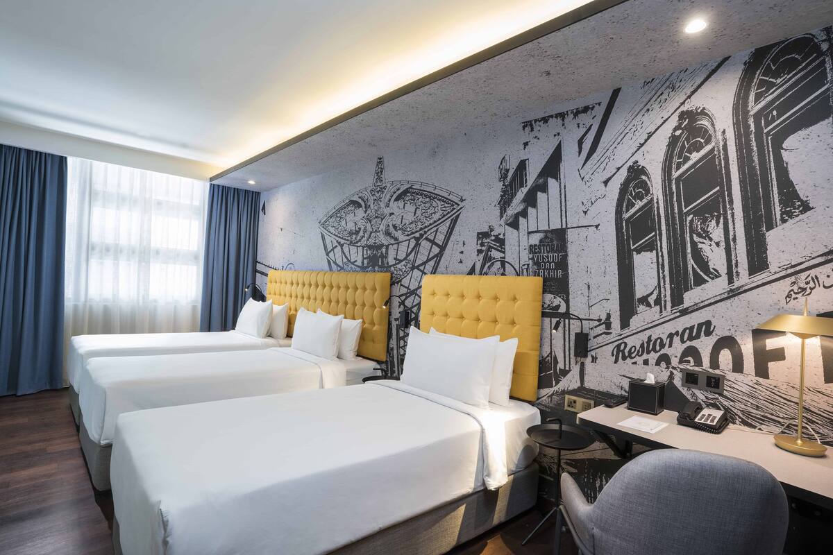Une chambre d’hôtel avec trois lits, un bureau, une chaise et une fresque murale.